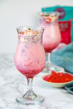 two glasses filled with liquid sitting on top of a white marble counter next to blue towels