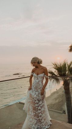 a woman standing on top of a cliff near the ocean wearing a dress with flowers