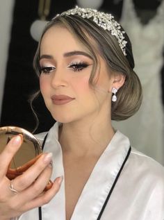 a woman wearing a tiara and holding a compact mirror in her hand while looking at it