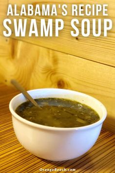 a white bowl filled with green soup on top of a wooden table next to a spoon