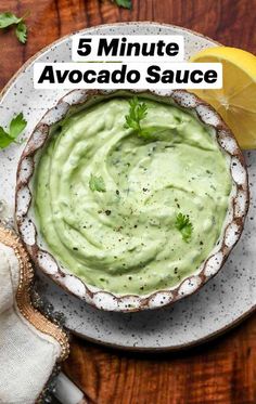 a white bowl filled with avocado sauce on top of a wooden table next to a lemon wedge