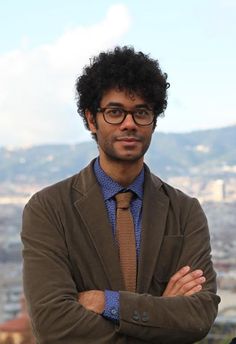 a man with his arms crossed standing in front of a cityscape and mountains