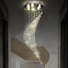 a modern chandelier hanging from the ceiling in a hallway with white walls and stairs