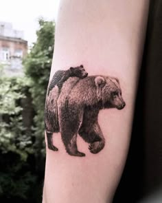 a bear and cub tattoo on the right arm, with trees in the back ground