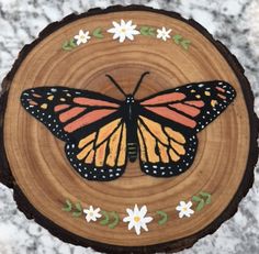 an orange and black butterfly sitting on top of a piece of wood with flowers around it