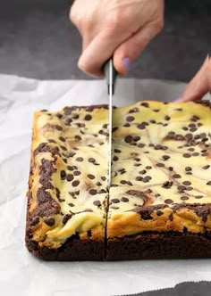 a person cutting into a cake with a knife on top of white paper and some chocolate chips