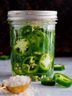 a jar filled with sliced green peppers on top of a white counter next to a spoon