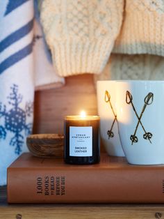 a candle sitting on top of a book next to a coffee cup and sweaters