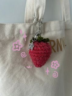 a crocheted strawberry keychain hanging from a tote bag