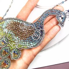 "This necklace was made a showpiece for the annual fair here in San Diego...it it large, gem-encrusted and not for the faint of heart! A fabulous hand-shaped peacock has been formed from various gauges of fine silver wire and meticulous wrapped together. The bird has been filled in with a plethora of varied gemstones: at his head are BLACK DIAMOND chips in his beak, BLACK SPINEL and MOONSTONE around his eye and his neck stretches out, populated with rich blue LONDON BLUE TOPAZ. At the crest of h Wire Wrapped Pendant Jewelry For Parties, Whimsical Pendant Jewelry For Party, Party Wire Wrapped Pendant Jewelry, Handmade Peacock Colored Jewelry For Weddings, Handmade Peacock Wedding Jewelry, Sterling Silver Necklace With Peacock Design, Silver Peacock Design Jewelry For Party, Bohemian Peacock Necklace As Gift, Bohemian Peacock Necklace For Gift