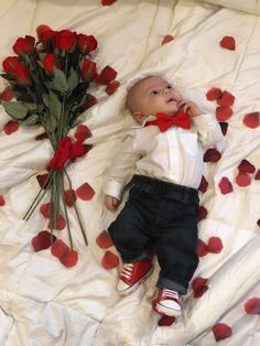 a baby laying on top of a bed next to red roses