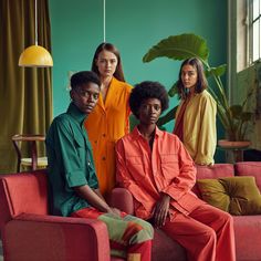 three women in orange and green outfits sitting on a red couch