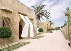 an alley way between two buildings with palm trees on either side and another building in the background