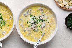 two white bowls filled with soup next to other foods on a table and spoons