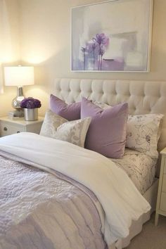 a white bed topped with lots of pillows next to a painting on the wall above it