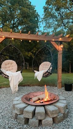 an outdoor fire pit with hanging chairs and lights on the top, surrounded by gravel