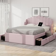 a pink bed with drawers underneath it and a laptop on the end table in front of it