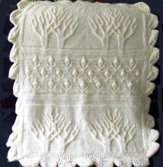 a white crocheted blanket on top of a wooden table next to a plant