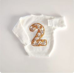 🌟 A Timeless Treasure: Hand-Embroidered Personalized Baby Sweater 🌟 Introducing our hand-embroidered personalized baby sweater, a timeless treasure that will warm your heart as much as it warms your little one. Made of the softest yarn and delicately personalized with your child's age, this sweater is more than just clothing--it's a symbol of love and a keepsake to be cherished for life. 🧶 Craftsmanship at Its Finest: Each sweater is meticulously hand-embroidered by our skilled artisans with White Tops For Birthday And Winter, White Top For Birthday In Winter, White Long Sleeve Tops For First Birthday, Embroidered Winter Birthday Sweater, Hand Embroidered Sweater, Baby Jumpers, Name Sweater, Baby Jumper, Toddler Sweater