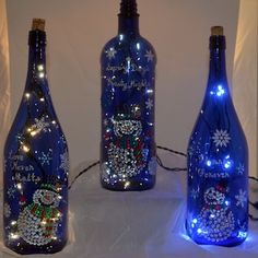 three blue bottles with lights on them and snowmen in the bottle are sitting next to each other