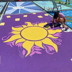 a woman is drawing on the ground with chalk and paint in front of an art project