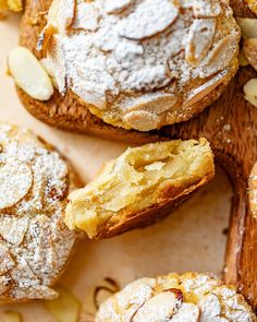 baked goods displayed on wooden cutting board with powdered sugar and almonds around them