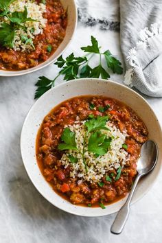 two bowls filled with chili and rice on top of a white countertop next to a spoon