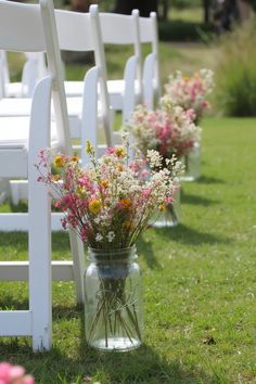 flowers in mason jars are lined up on the grass at an outdoor ceremony with white chairs