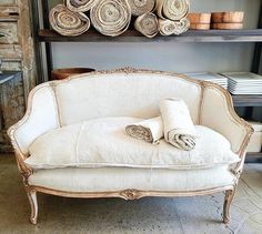 a white couch with rolled up blankets on it in front of a shelf filled with stacks of folded towels