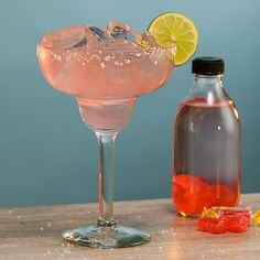 a pink drink in a glass next to a bottle of alcohol on a wooden table