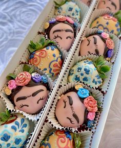 there are many chocolates in the box with faces painted on them and decorated with flowers