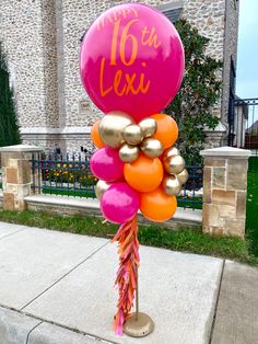 a bunch of balloons that are on a pole in front of a house with the number sixteen six written on it