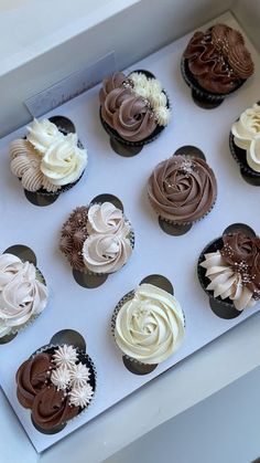 twelve cupcakes with white and chocolate frosting in a box on a table