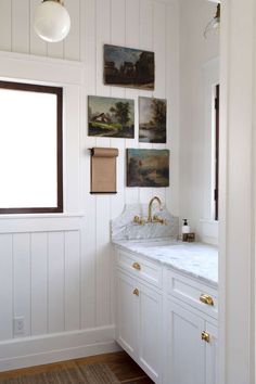 a bathroom with white cabinets and paintings on the wall