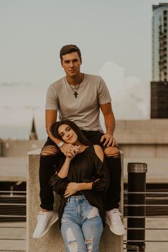 two people sitting on top of each other in front of a tall building and one person standing behind them