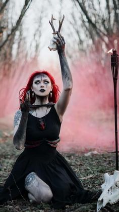 a woman with red hair and makeup sitting on the ground holding up two horns in front of her face