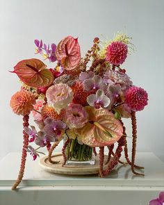 a vase filled with lots of pink and purple flowers on top of a white table