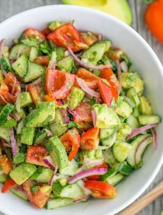 a white bowl filled with cucumber, tomato and onion salad on top of a wooden table