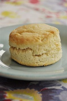 a biscuit on a blue plate sitting on a floral tablecloth covered table cloth