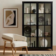 a black bookcase with glass doors is in the living room next to a white chair