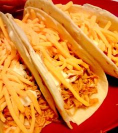 three tacos with shredded cheese on a red plate