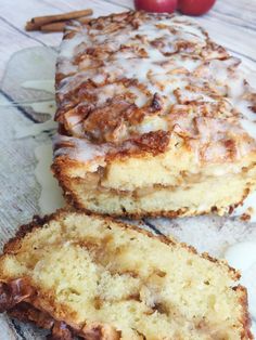 a loaf of cinnamon apple bread with icing next to two apples on a table