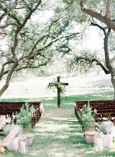 an outdoor wedding setup with wooden chairs and greenery on the aisle, surrounded by trees