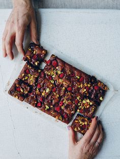 two hands reaching for a piece of cake on top of a white table with red and yellow toppings