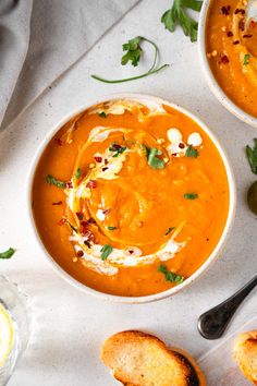 two bowls of carrot soup with bread and garnishes on the side next to spoons