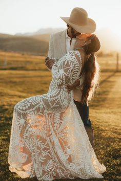 a woman in a white dress and cowboy hat kissing her man on the cheek while he is