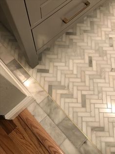 a kitchen floor with white and grey herringbone tile on it, next to a cabinet