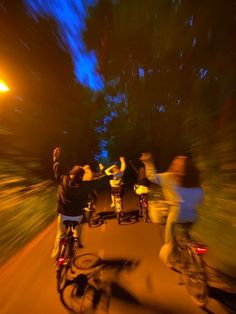 several people riding bikes down a street at night time with their arms in the air