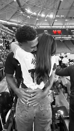 a man and woman embracing in the stands at a sporting event with red hearts on their shirts