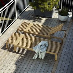 an empty wooden deck with two chairs and a blanket on the ground next to a potted tree